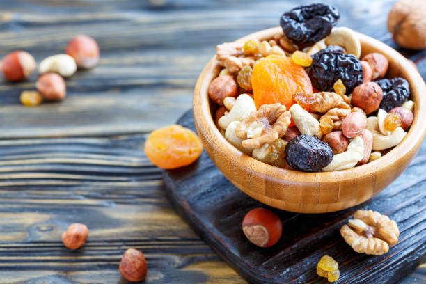 Bowl with a mixture of dried fruit and nuts on an old kitchen table, selective focus.